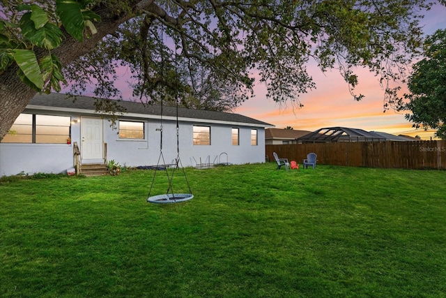 back of house at dusk with entry steps, stucco siding, fence, and a lawn