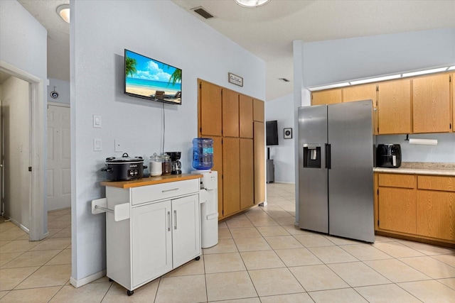 kitchen with lofted ceiling, light tile patterned flooring, visible vents, light countertops, and stainless steel fridge with ice dispenser