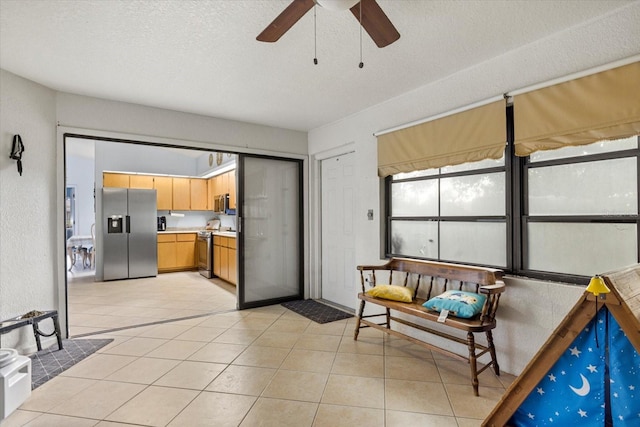 interior space with a textured ceiling, light tile patterned flooring, stainless steel appliances, a ceiling fan, and light countertops