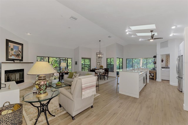 living room featuring lofted ceiling with skylight, sink, light hardwood / wood-style flooring, and ceiling fan with notable chandelier