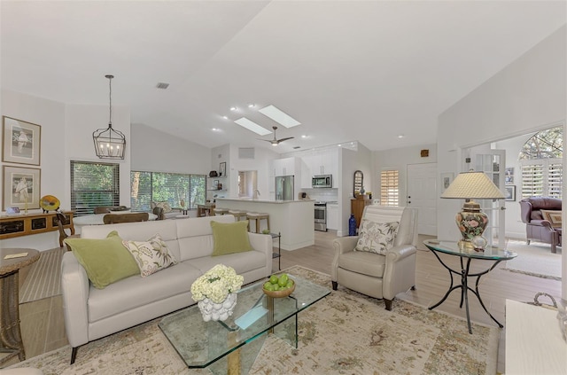 living room featuring a chandelier, light wood-type flooring, a healthy amount of sunlight, and a skylight