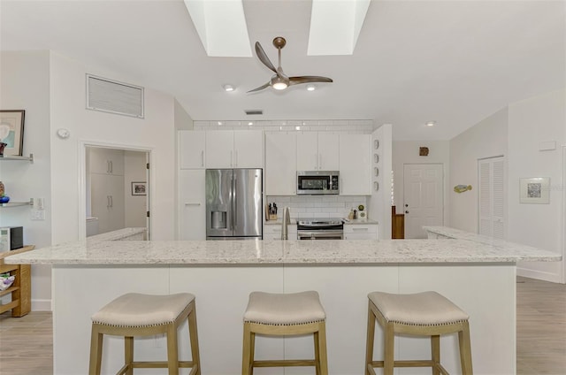 kitchen featuring light hardwood / wood-style flooring, stainless steel appliances, white cabinetry, light stone counters, and a skylight