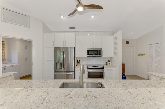 kitchen with light stone counters, white cabinetry, independent washer and dryer, sink, and stainless steel appliances