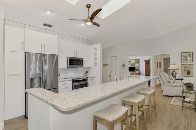 kitchen featuring appliances with stainless steel finishes, white cabinetry, a kitchen bar, light hardwood / wood-style flooring, and lofted ceiling with skylight