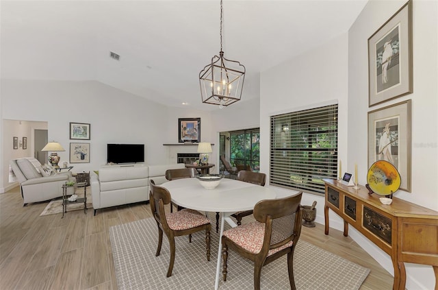 dining area with a chandelier, light wood-type flooring, and vaulted ceiling