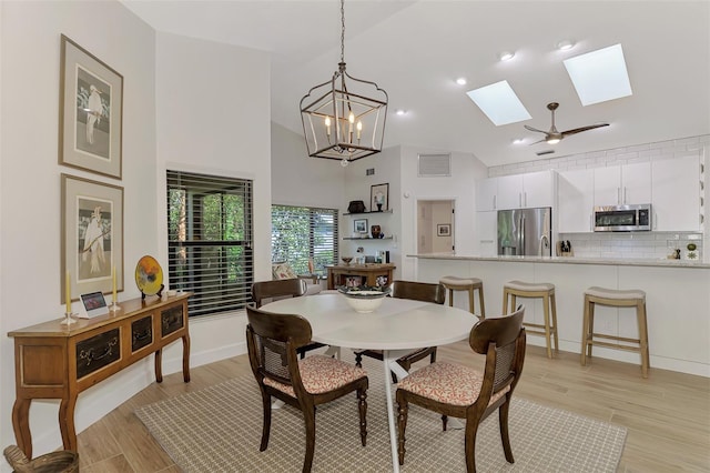 dining space featuring a towering ceiling, light hardwood / wood-style flooring, ceiling fan with notable chandelier, and a skylight