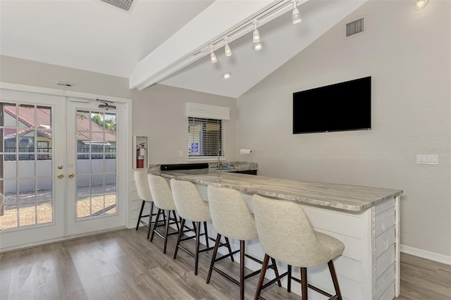 bar featuring lofted ceiling, french doors, light hardwood / wood-style flooring, sink, and light stone countertops