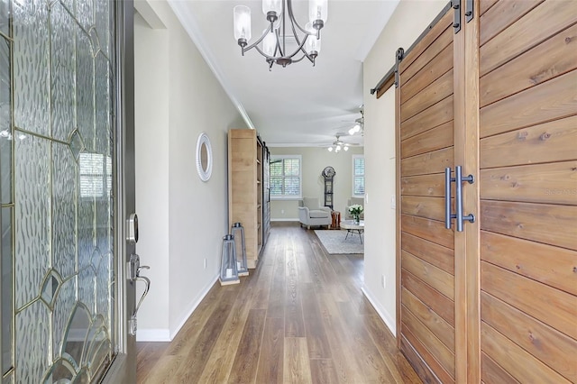 entrance foyer featuring ceiling fan with notable chandelier, crown molding, a barn door, and dark hardwood / wood-style floors