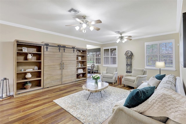 living room featuring crown molding, a barn door, hardwood / wood-style flooring, and ceiling fan