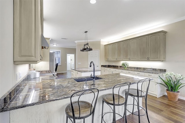 kitchen with crown molding, hardwood / wood-style flooring, sink, and an island with sink