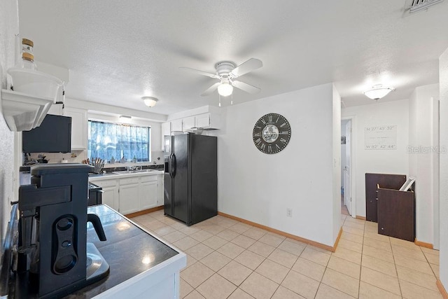 kitchen featuring black fridge with ice dispenser, ceiling fan, sink, light tile patterned floors, and white cabinetry