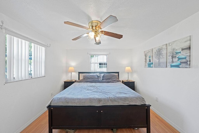 bedroom with a textured ceiling, ceiling fan, light hardwood / wood-style flooring, and multiple windows