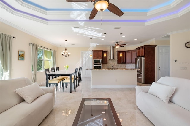 living room with ceiling fan with notable chandelier, ornamental molding, and a tray ceiling