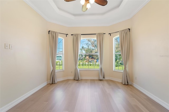 unfurnished room featuring a raised ceiling, ceiling fan, plenty of natural light, and light wood-type flooring