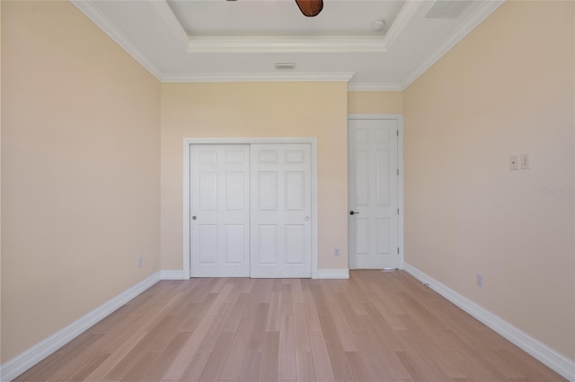 unfurnished bedroom featuring a raised ceiling, crown molding, a closet, and light hardwood / wood-style floors