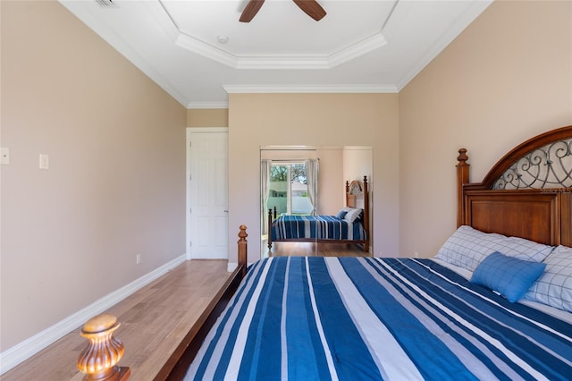 bedroom featuring ceiling fan, wood-type flooring, ornamental molding, and a tray ceiling