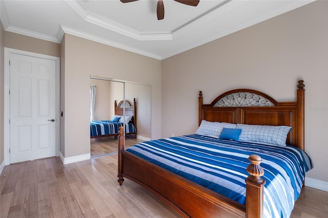 bedroom with light hardwood / wood-style flooring, ceiling fan, ornamental molding, a tray ceiling, and a closet