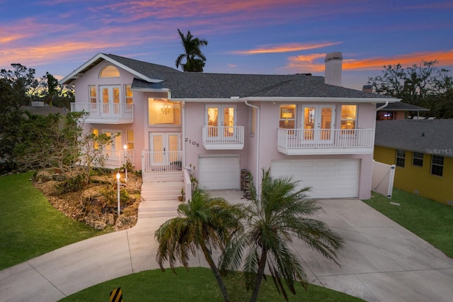 view of front of home featuring french doors, a balcony, a garage, and a lawn