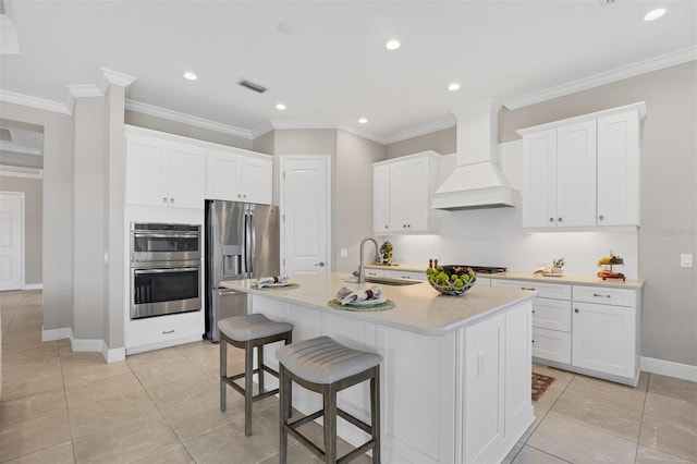 kitchen featuring stainless steel appliances, sink, a kitchen island with sink, white cabinetry, and premium range hood