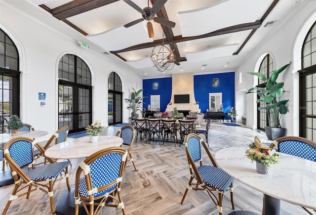 dining area with a towering ceiling, ceiling fan with notable chandelier, a fireplace, and ornamental molding