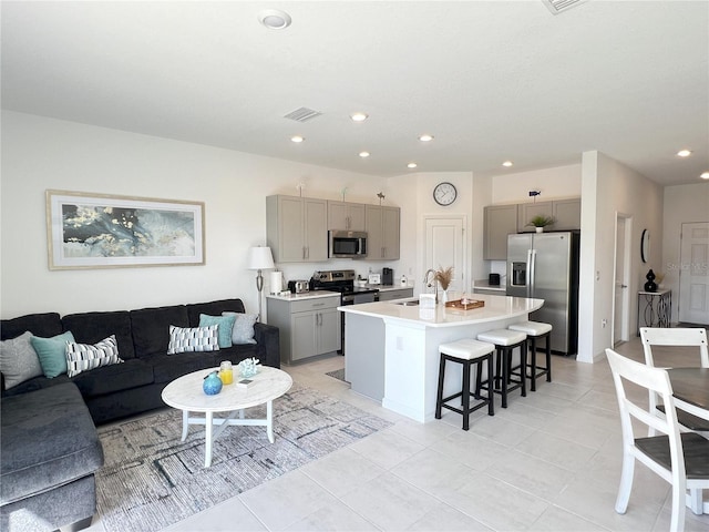 kitchen with appliances with stainless steel finishes, a kitchen breakfast bar, a kitchen island with sink, gray cabinets, and sink