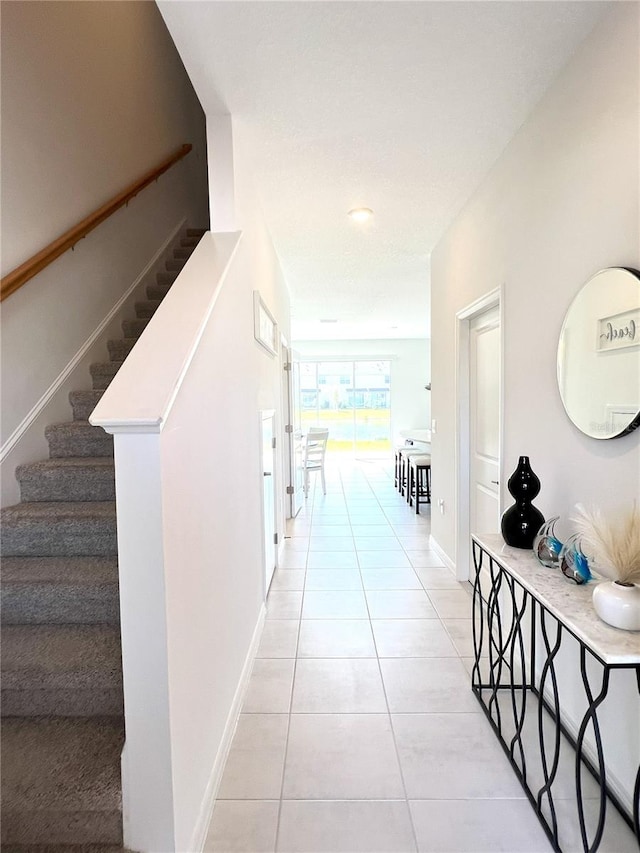 hall with stairway, light tile patterned flooring, and baseboards