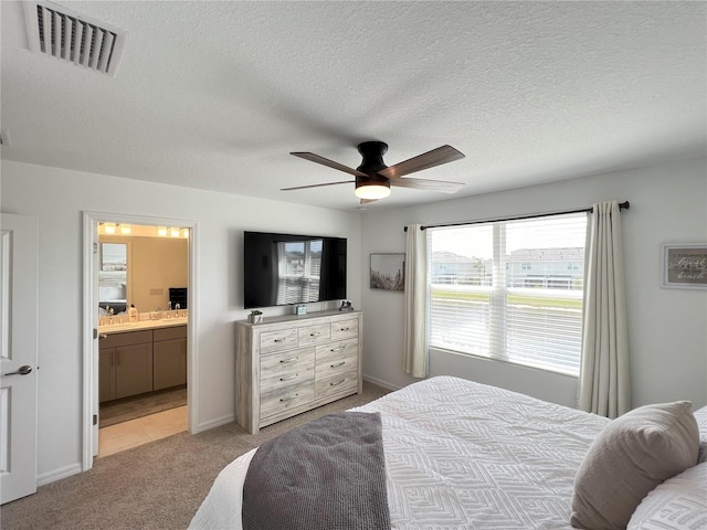 bedroom featuring ceiling fan, a textured ceiling, light carpet, visible vents, and ensuite bath