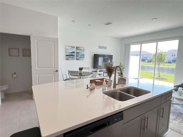 kitchen with light tile patterned floors, a sink, visible vents, dishwasher, and a center island with sink