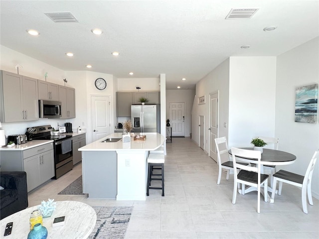 kitchen featuring appliances with stainless steel finishes, gray cabinets, and a kitchen island with sink