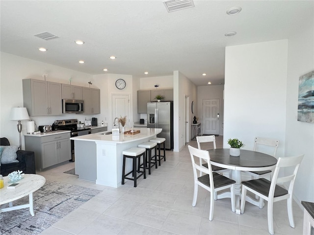 kitchen with an island with sink, gray cabinetry, sink, a breakfast bar, and appliances with stainless steel finishes