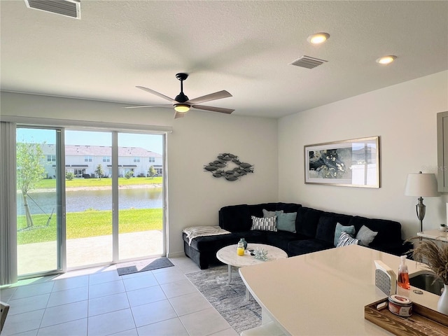 living area featuring visible vents, a water view, a textured ceiling, and light tile patterned floors