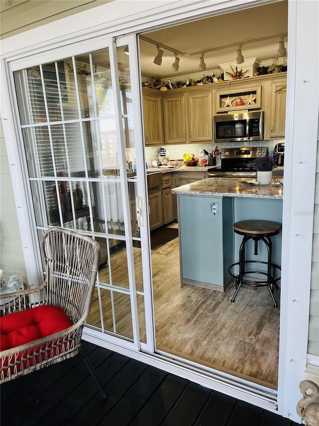 kitchen with light wood-type flooring, appliances with stainless steel finishes, a breakfast bar, and stone countertops