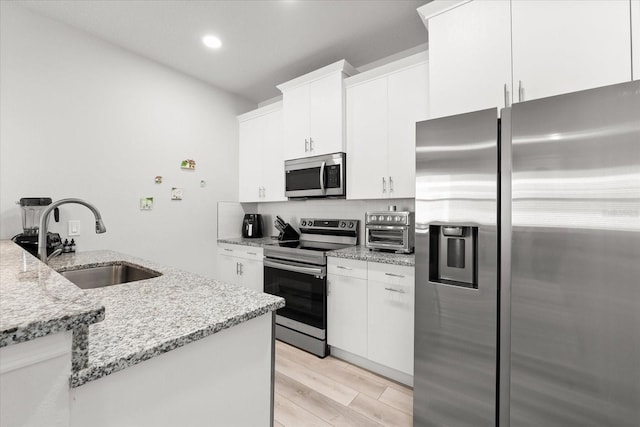 kitchen featuring white cabinets, light hardwood / wood-style flooring, sink, light stone countertops, and appliances with stainless steel finishes