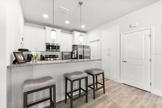 kitchen with light wood-type flooring, white cabinetry, appliances with stainless steel finishes, decorative light fixtures, and kitchen peninsula