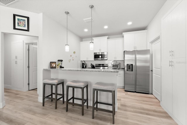 kitchen with white cabinetry, kitchen peninsula, appliances with stainless steel finishes, light stone countertops, and light wood-type flooring