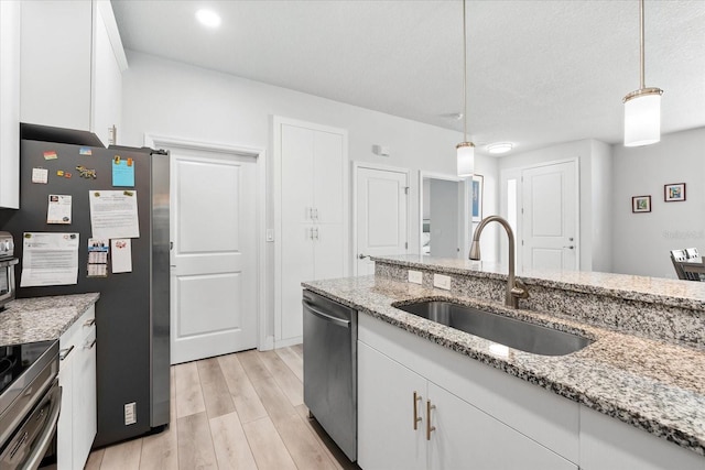 kitchen with stainless steel appliances, sink, decorative light fixtures, light hardwood / wood-style flooring, and white cabinets