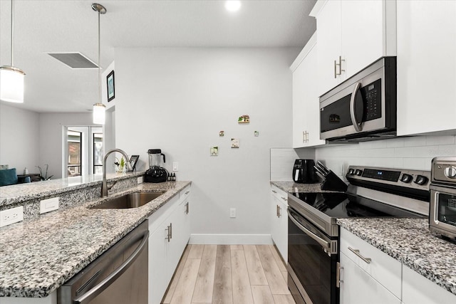 kitchen with stainless steel appliances, white cabinetry, sink, decorative light fixtures, and light wood-type flooring