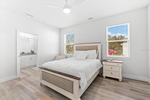 bedroom with ensuite bath, ceiling fan, multiple windows, and light hardwood / wood-style flooring