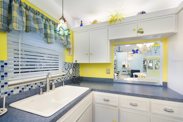 kitchen with an inviting chandelier, white cabinetry, sink, and backsplash