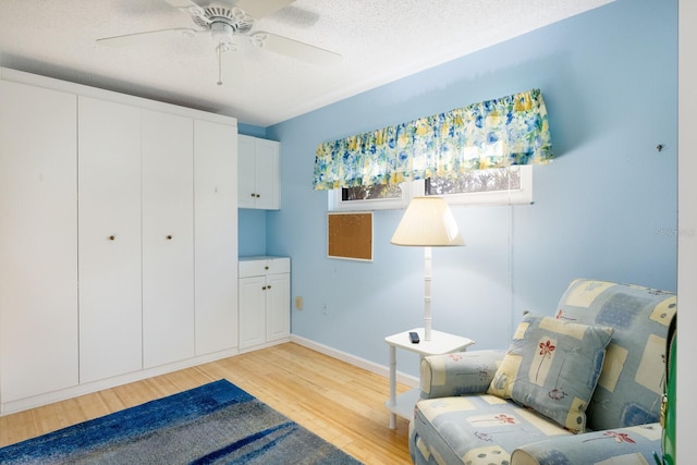 living area featuring light hardwood / wood-style flooring, a textured ceiling, and ceiling fan