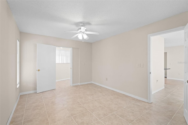 empty room featuring a textured ceiling, light tile patterned floors, and ceiling fan