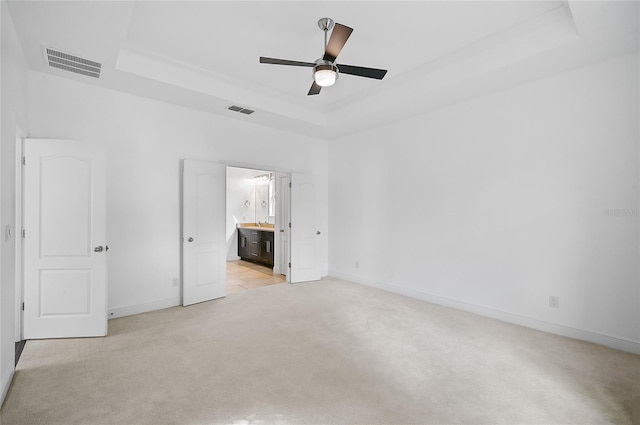 unfurnished bedroom with ceiling fan, ensuite bath, light carpet, and a tray ceiling