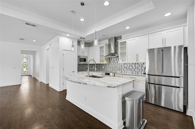 kitchen featuring stainless steel appliances, white cabinetry, wall chimney exhaust hood, an island with sink, and hanging light fixtures