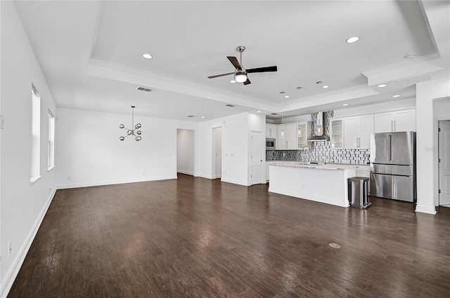 unfurnished living room with sink, ornamental molding, dark hardwood / wood-style floors, ceiling fan with notable chandelier, and a raised ceiling