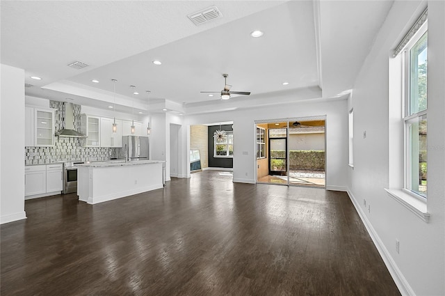 unfurnished living room featuring dark wood-type flooring, a healthy amount of sunlight, ceiling fan, and a tray ceiling