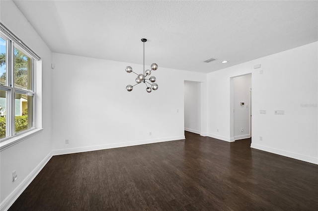 empty room with a chandelier, a textured ceiling, and dark hardwood / wood-style floors