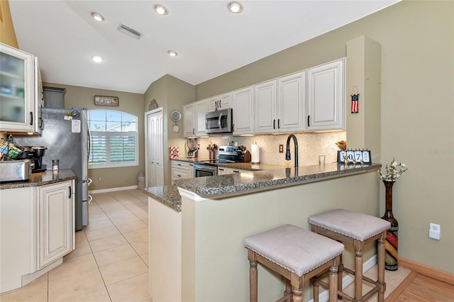 kitchen featuring white cabinetry, kitchen peninsula, stainless steel appliances, and dark stone counters