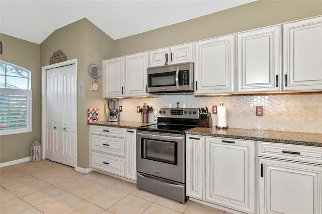 kitchen featuring light tile patterned flooring, white cabinetry, appliances with stainless steel finishes, dark stone countertops, and vaulted ceiling