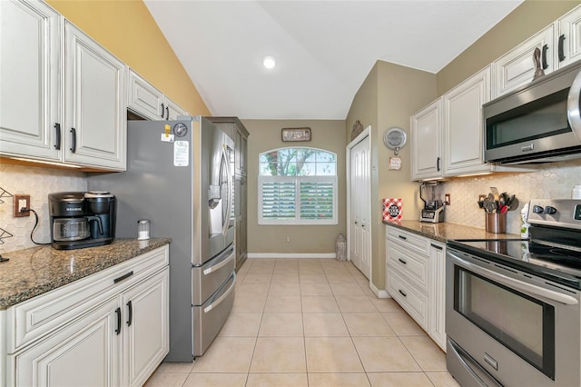 kitchen with white cabinets, appliances with stainless steel finishes, dark stone countertops, and vaulted ceiling