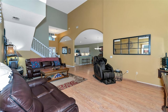 living room featuring an inviting chandelier, light hardwood / wood-style floors, and a towering ceiling